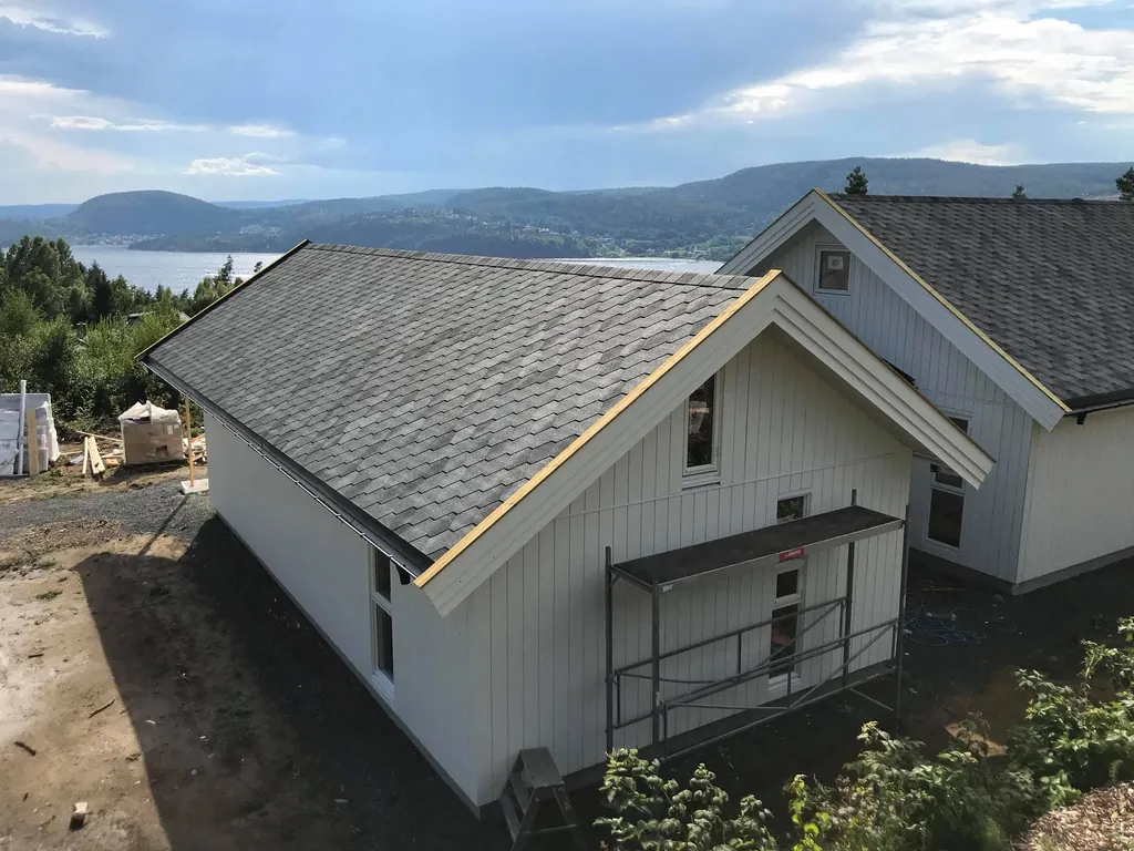 Hvitt hus med grå takshingel og utsikt over vann og åser