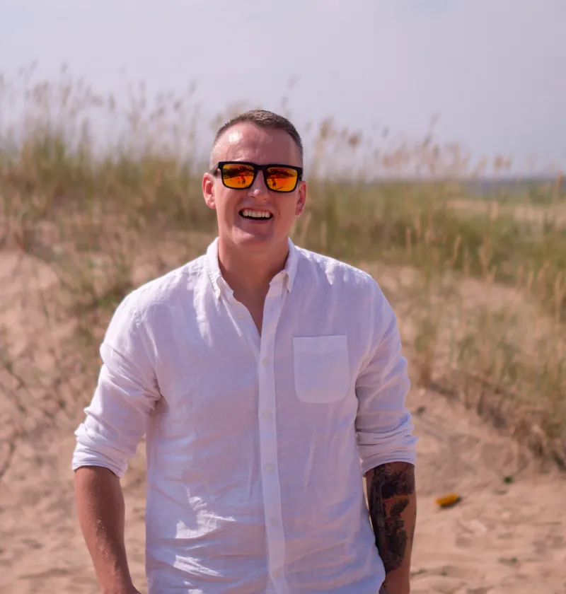 Janis Martins i hvit skjorte, smilende på en strand