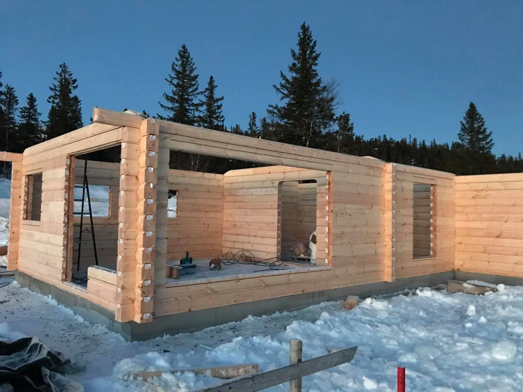 Laftede tømmervegger reises på en tomt med snø