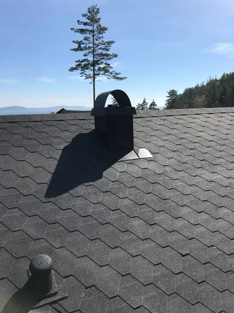 Mørk takshingel og pipe under blå himmel